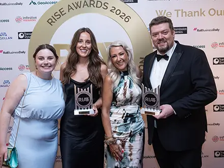 Four people in formal attire stand in front of a “RISE Awards 2026” backdrop, holding two glass awards with the “RIA” logo, surrounded by sponsor logos.