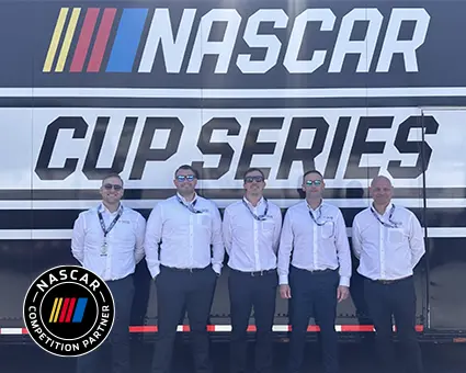 Five people wearing white shirts, stood in front of NASCAR signage