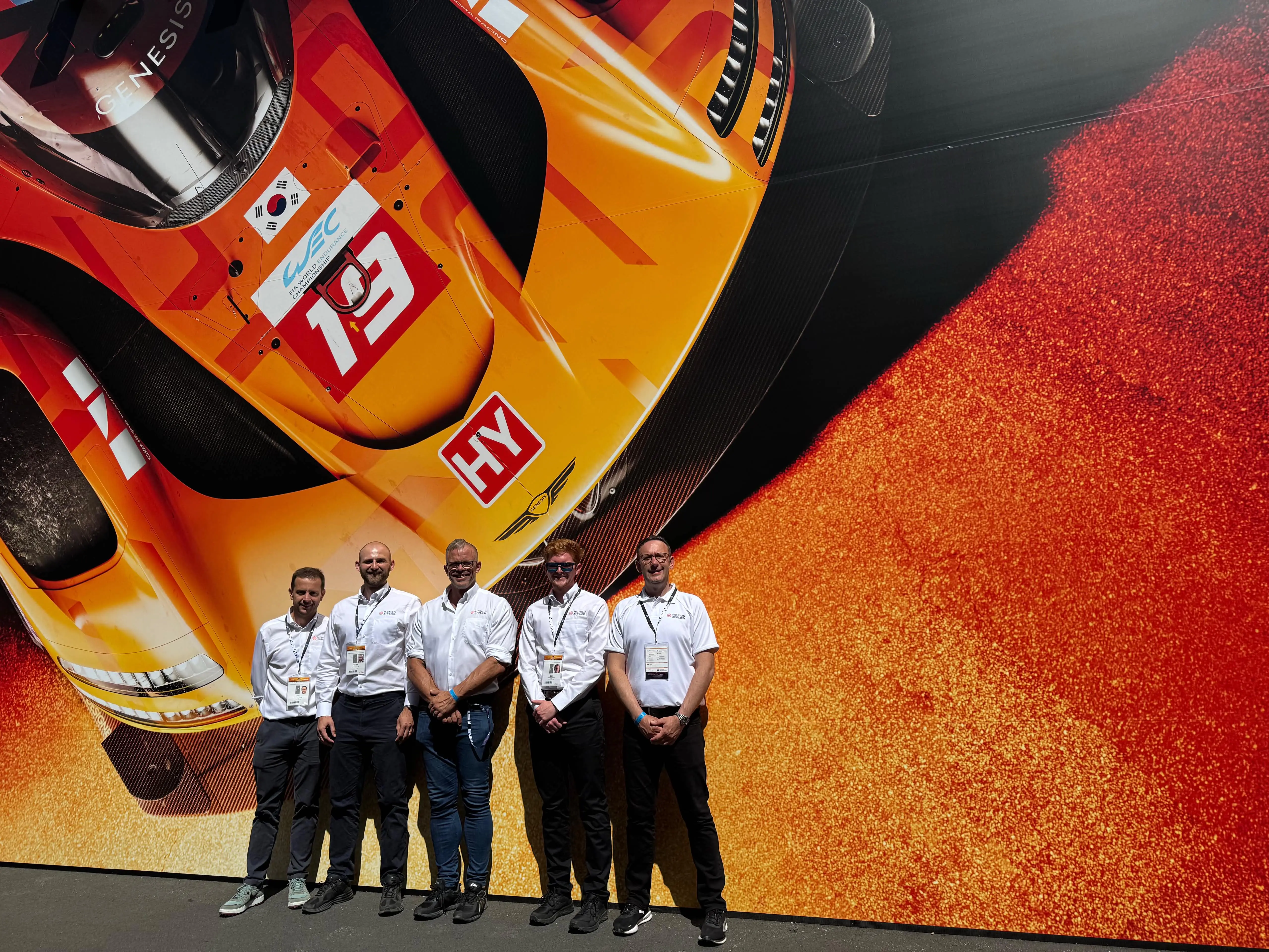 Five people stood wearing white shirts in front of a display showing an orange hypercar